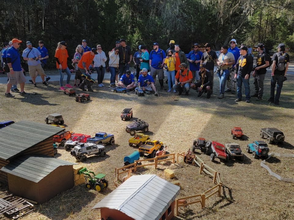 Veterans and families standing behind dozens of RC crawlers on a backyard course