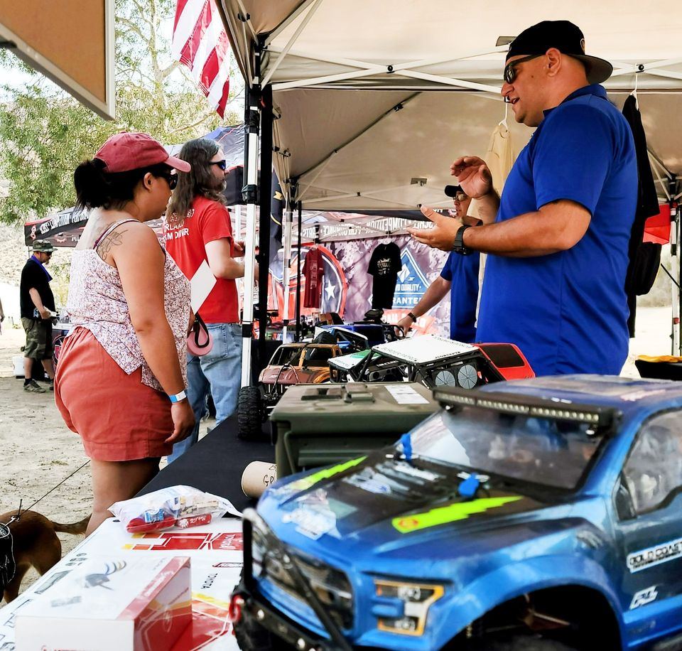 An O11C volunteer showing an RC truck to visitors at an event booth